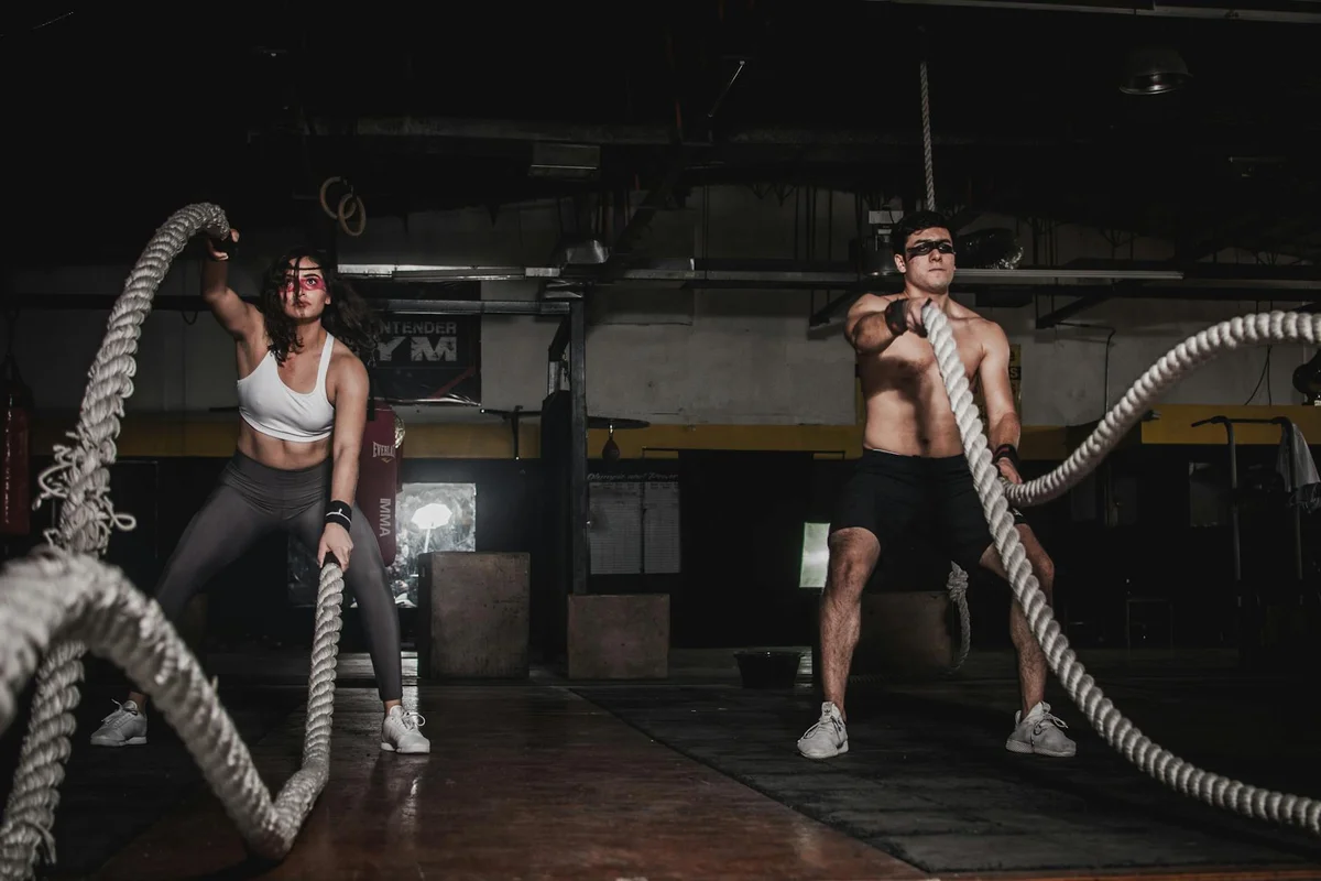 Two people using battle ropes in a garage gym with dark lighting, showcasing common equipment in a home workout space.