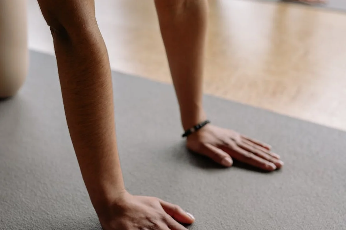 Close-up of a person’s hands placed on a gray gym mat, ready to install or position rubber flooring in a garage gym.