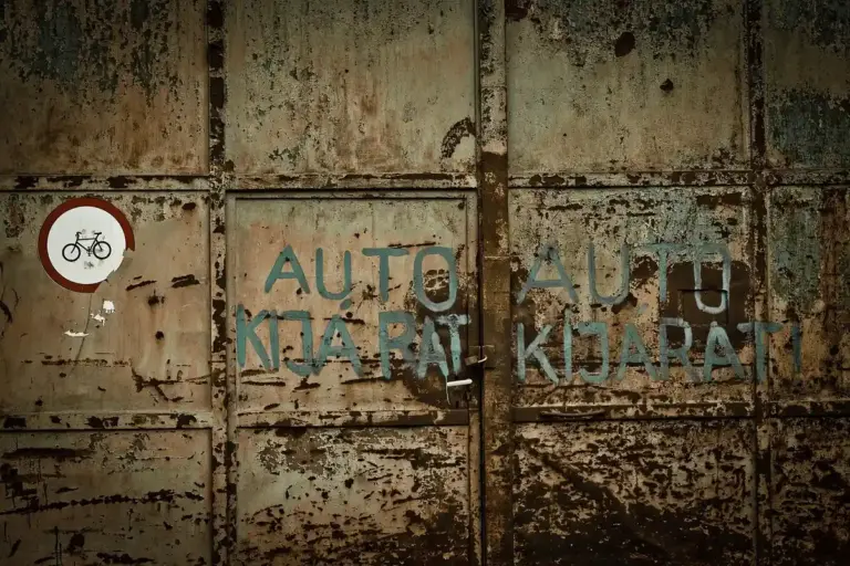 Rusty, weathered garage door with faded blue graffiti and a small circular bicycle sign on the left, suggesting a space ripe for conversion.