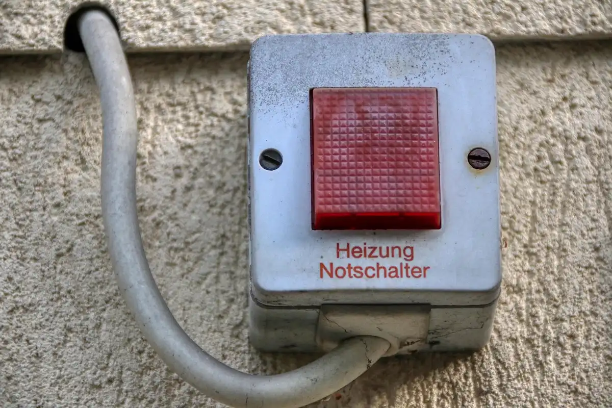 Red emergency shutoff switch labeled 'Heizung Notschalter' mounted on a beige exterior wall with a curved conduit