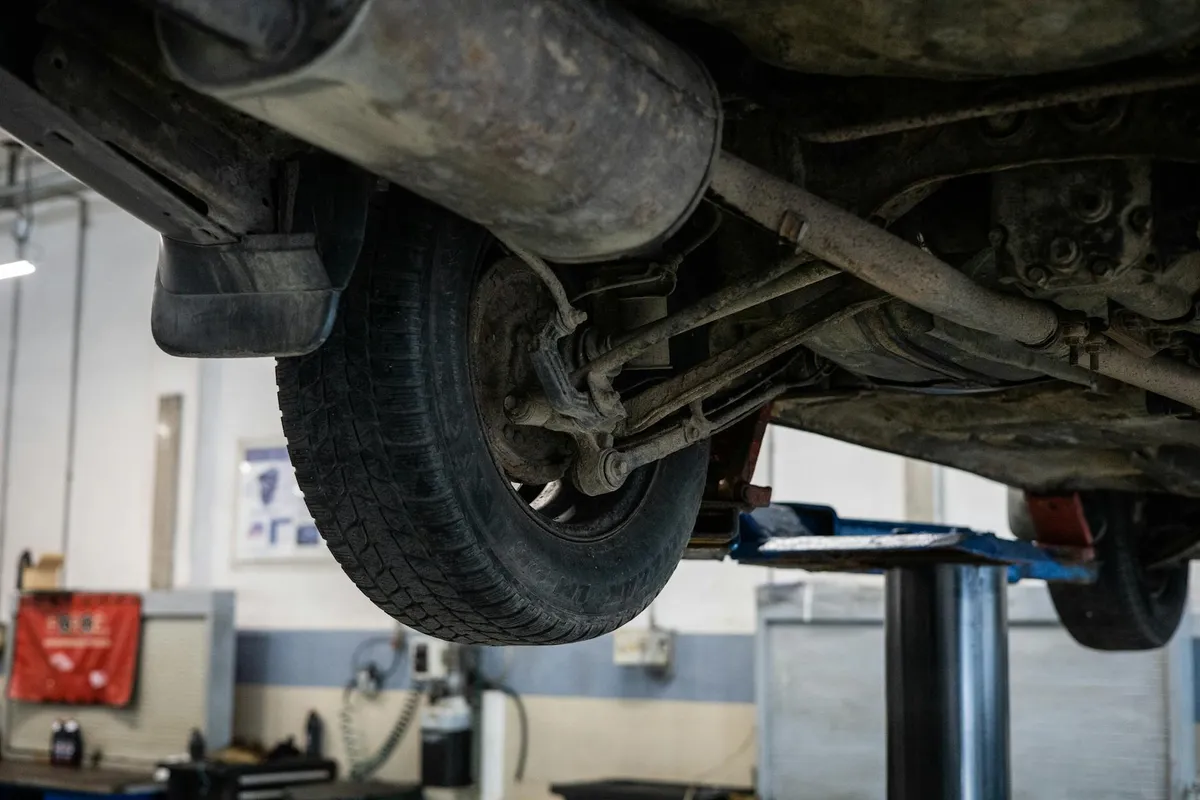 Underside of a car on a hydraulic lift in a workshop, showing the wheel and suspension components