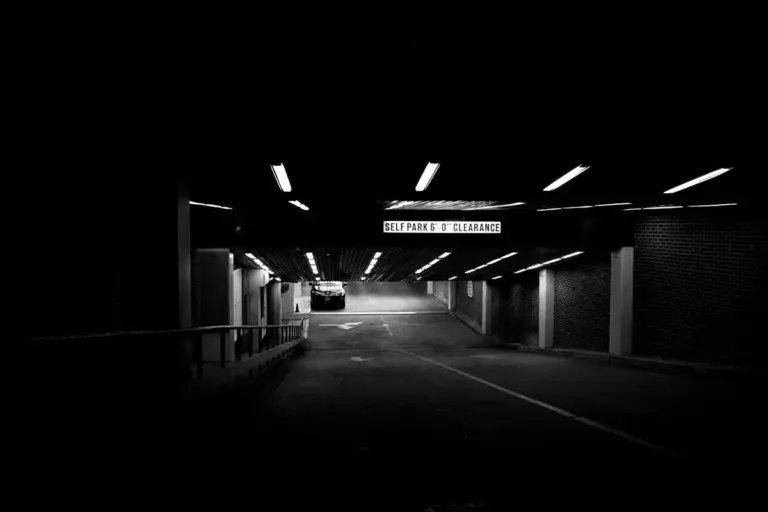 Dimly lit underground parking garage with overhead fluorescent lights and a car visible in the distance.
