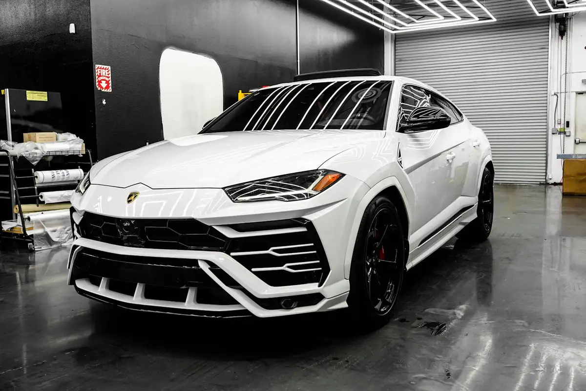 White Lamborghini Urus parked in a clean, modern garage with a polished concrete floor and organized tools.
