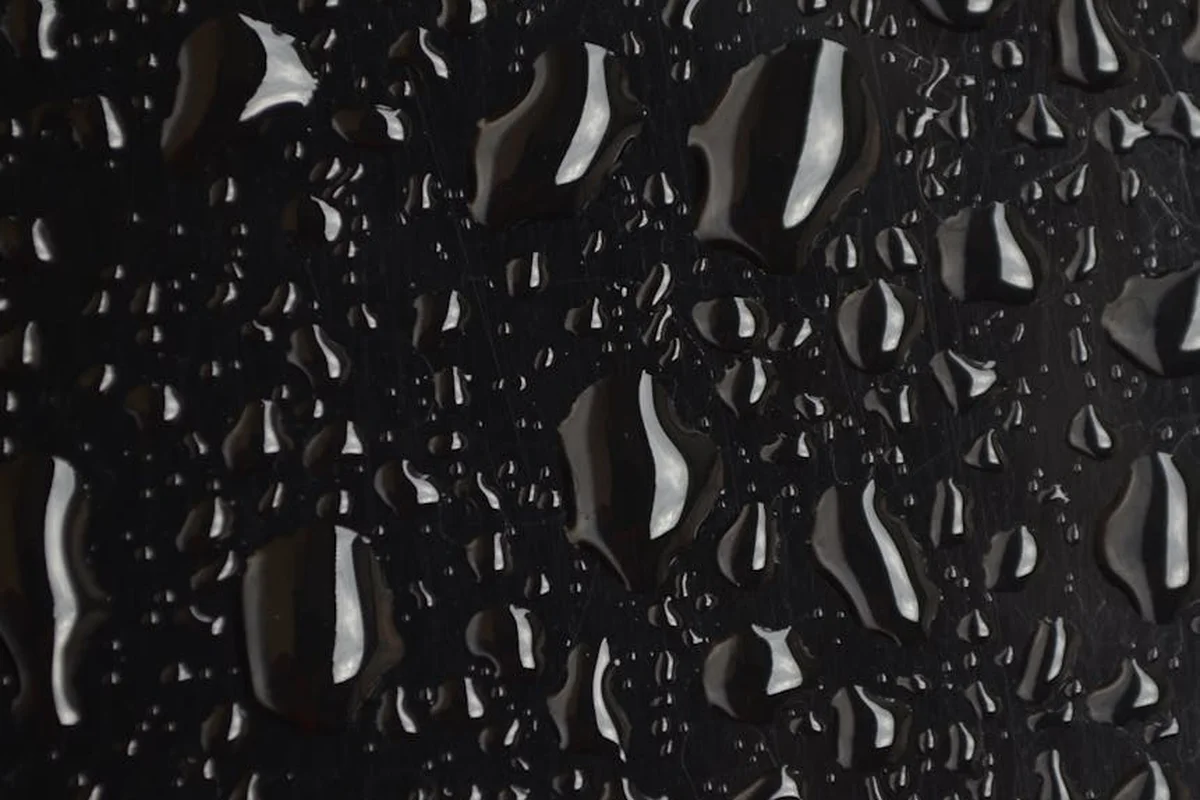 Close-up of moisture droplets on a dark, glossy surface, illustrating moisture challenges in garage concrete before flooring installation.