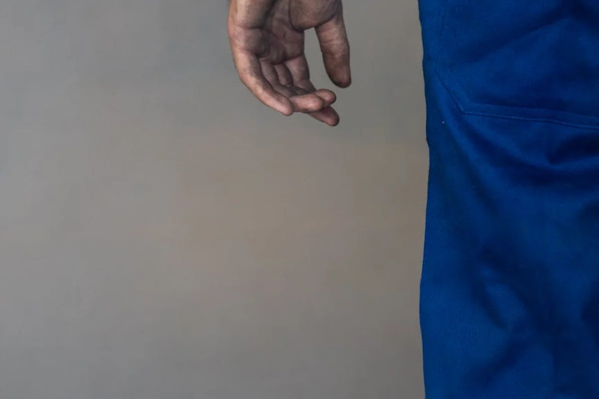 Close-up of a worker's hand wearing blue coveralls against a neutral wall