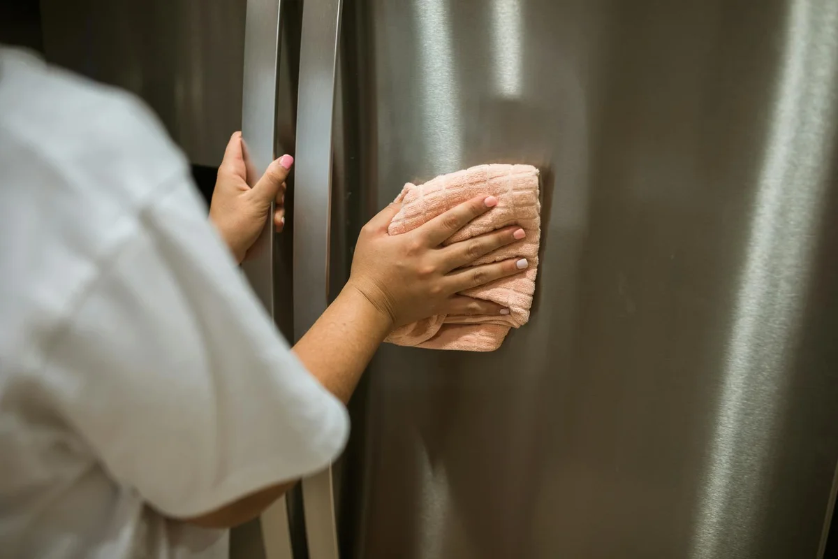 Hand wiping a stainless steel refrigerator door with a cloth