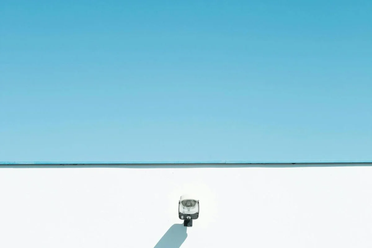 Exterior security camera mounted on a white garage wall with a clear blue sky above.