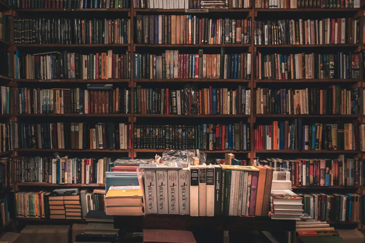 Dense wooden bookshelves filled with books, with a table cluttered with more books in the foreground.