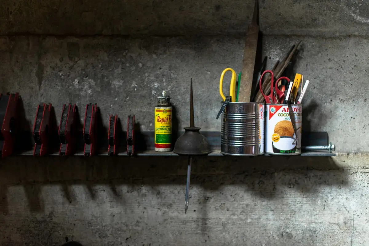 A cluttered garage shelf against a concrete wall holding various tools, cans, and containers, illustrating risks of storing furniture and wood in a garage.