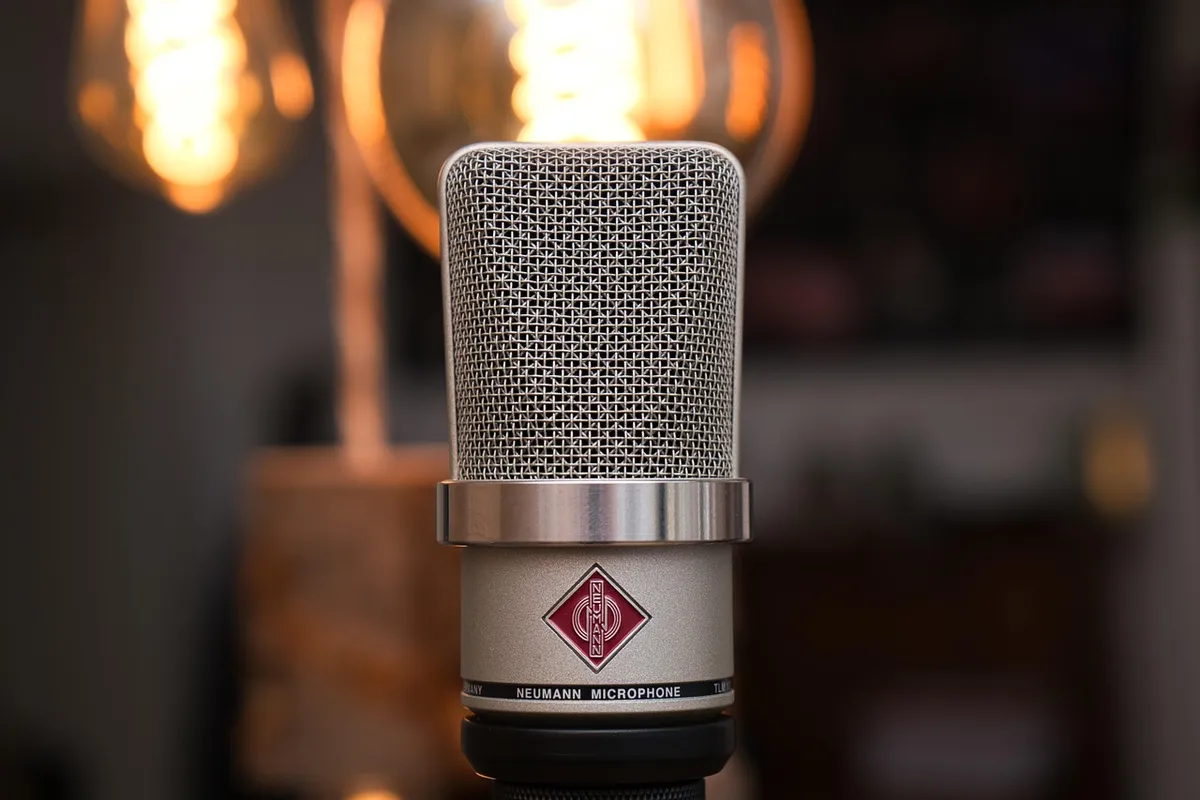 Close-up of a large-diaphragm condenser microphone mounted on a stand in a dimly lit garage studio with warm background lights
