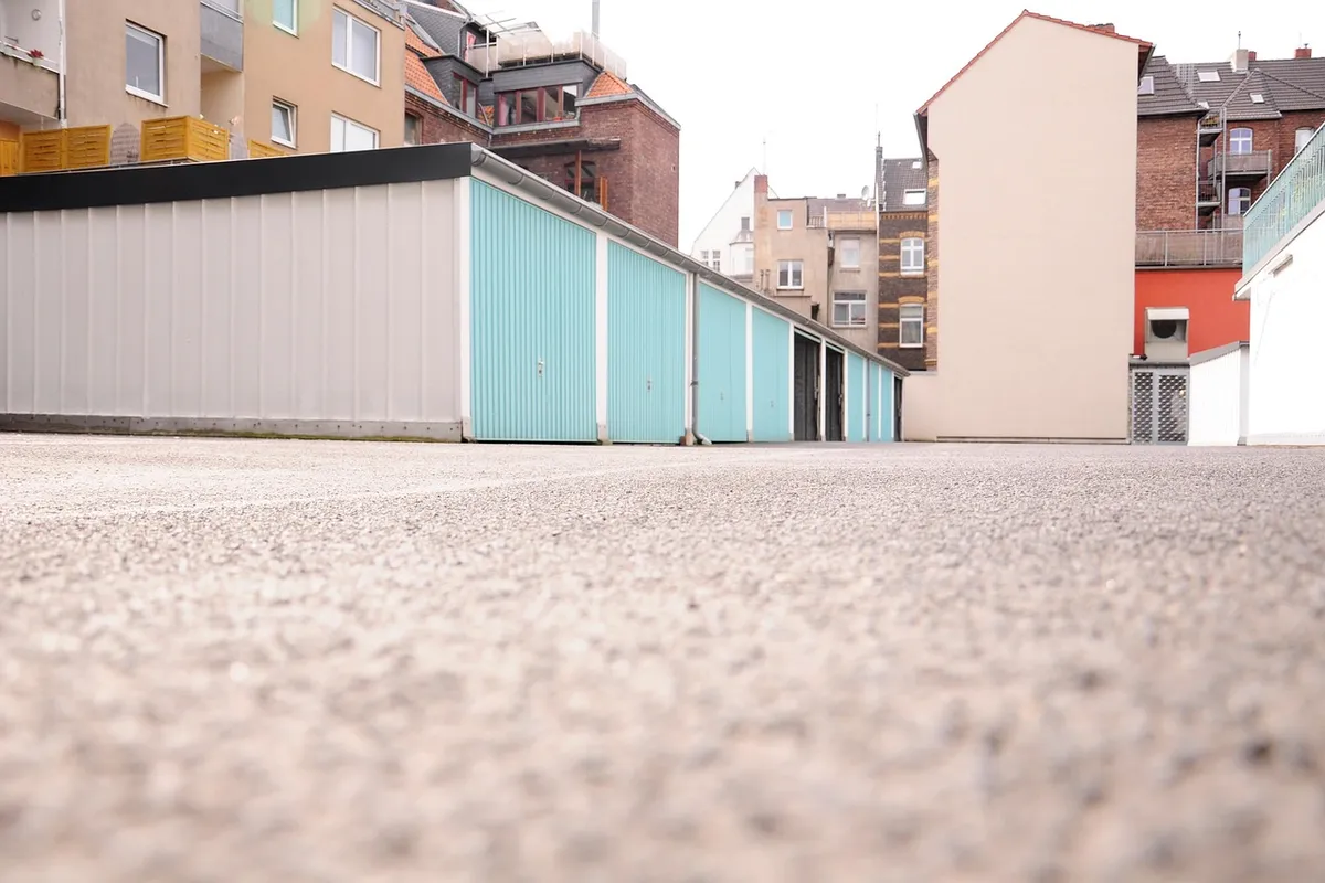Low-angle view of a row of storage garages with colorful doors along a concrete ground.