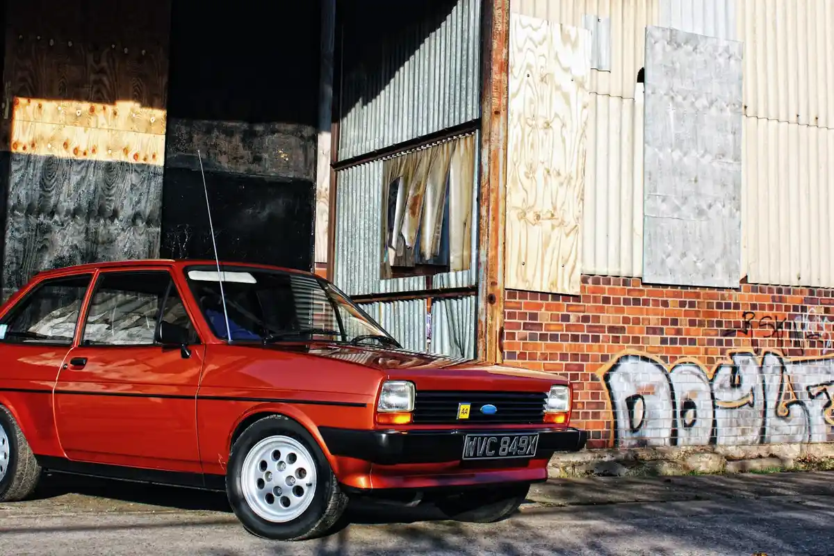 Red vintage car parked beside a graffiti-covered garage wall with boarded panels