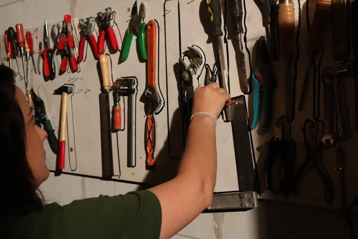 A person reaching for a tool on a pegboard wall filled with hand tools in a workshop, preparing to frame a wall.