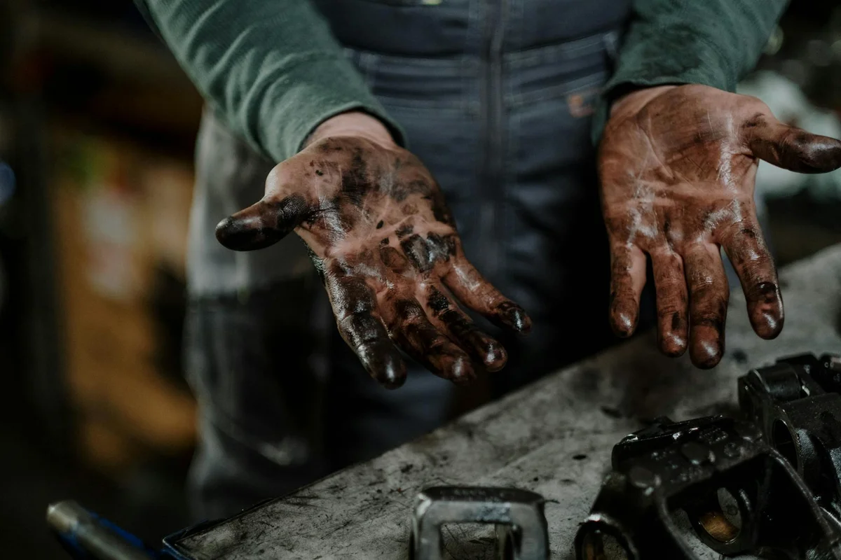 Close-up of muddy hands on a workbench with tools, suggesting a DIY garage project and hands-on decision making.