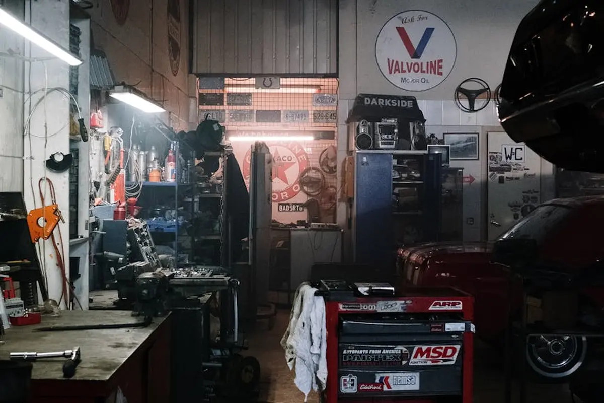 Cluttered home garage/workshop with a vehicle on a lift, tool cabinets, and shelves, illustrating a shared-space parking layout for motorcycles and small vehicles.