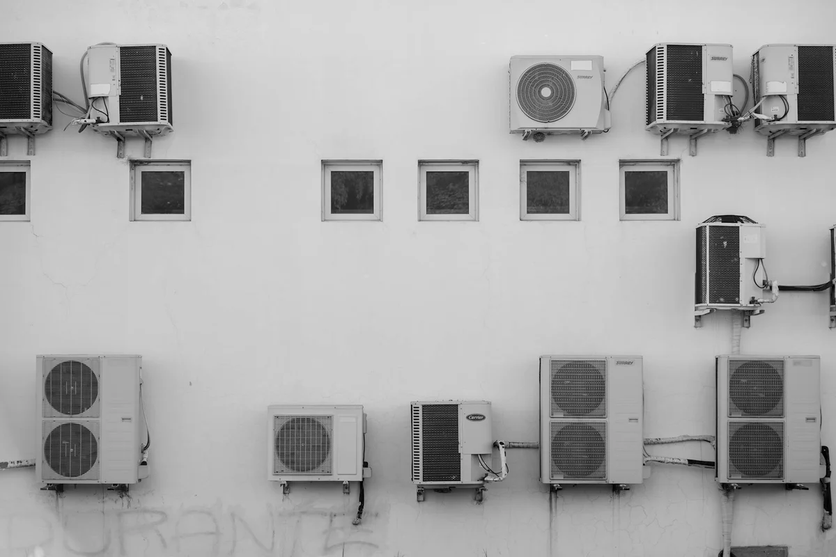 Black-and-white photo of multiple outdoor air conditioning units mounted on a white wall.