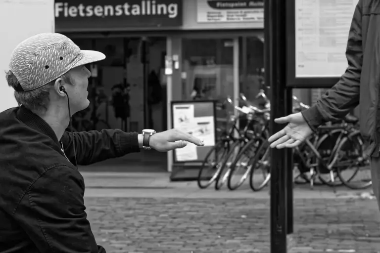 Person in a helmet and jacket extending a hand to another person outside a bike shop, with bicycles visible in the background.