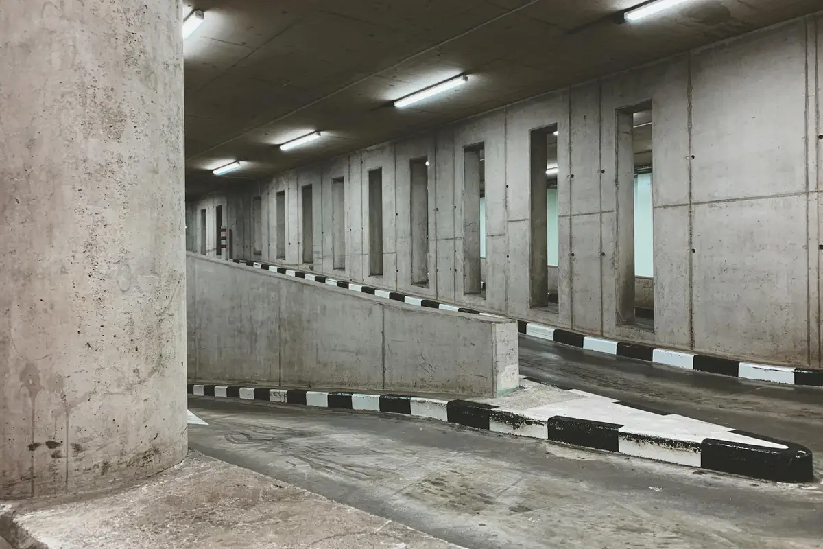 A concrete parking garage with large columns, a curved ramp, and painted curb edges, showcasing industrial gray walls and utilitarian lighting.