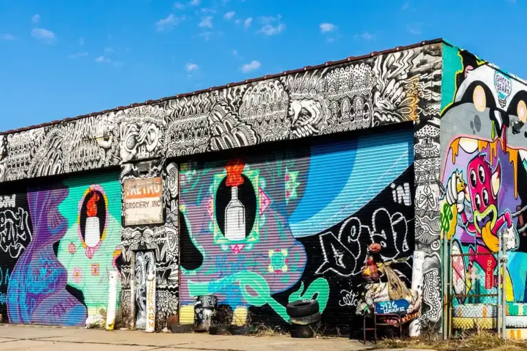 A graffiti-covered garage with colorful murals on its roll-up doors; a person stands near the right side of the building.