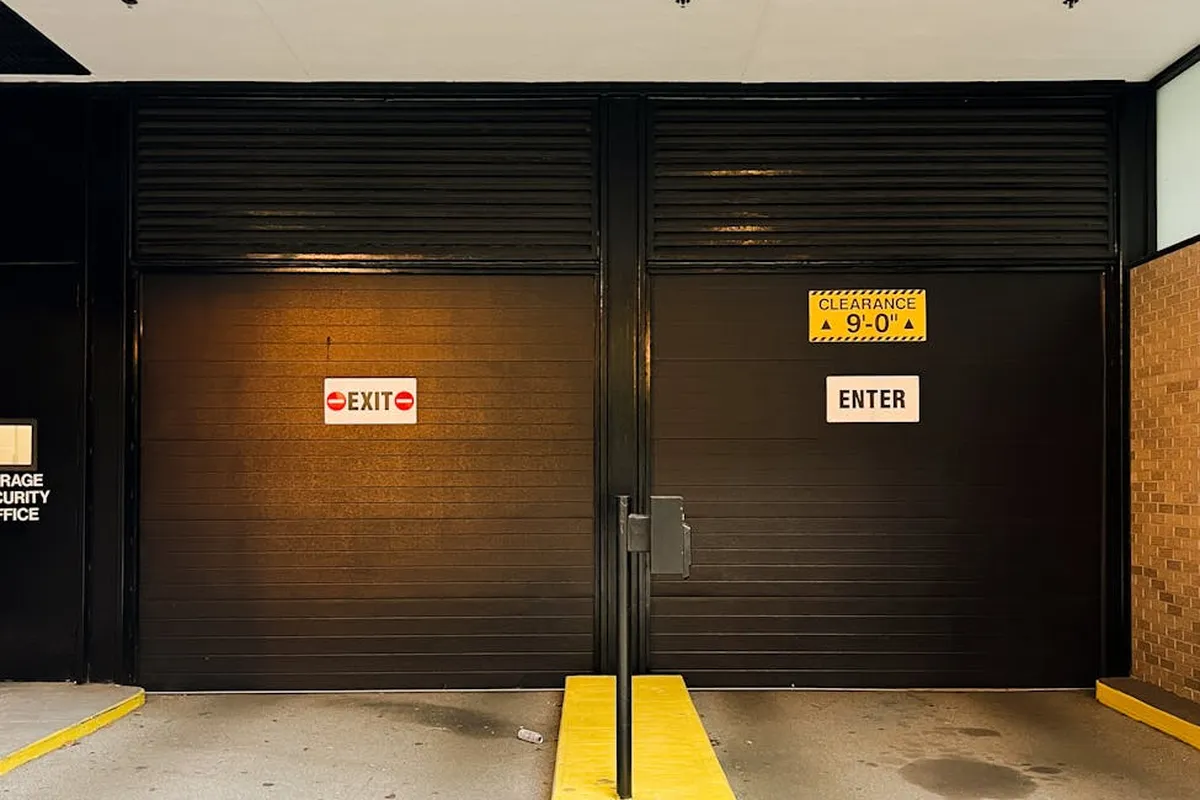 Black metal garage doors with a bright yellow curb, exit and enter signs, and clearance notice on the doors.