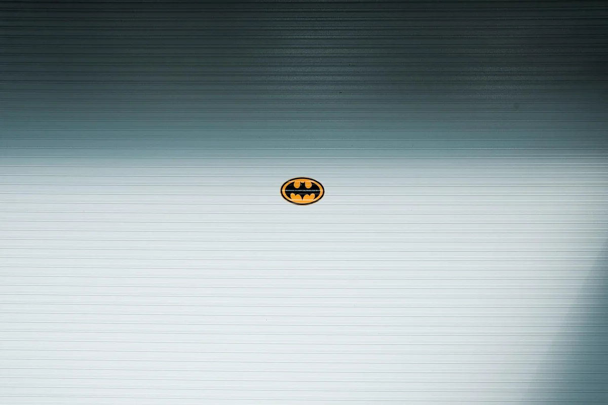 Close-up of a silver garage door panel with a small Batman emblem centered
