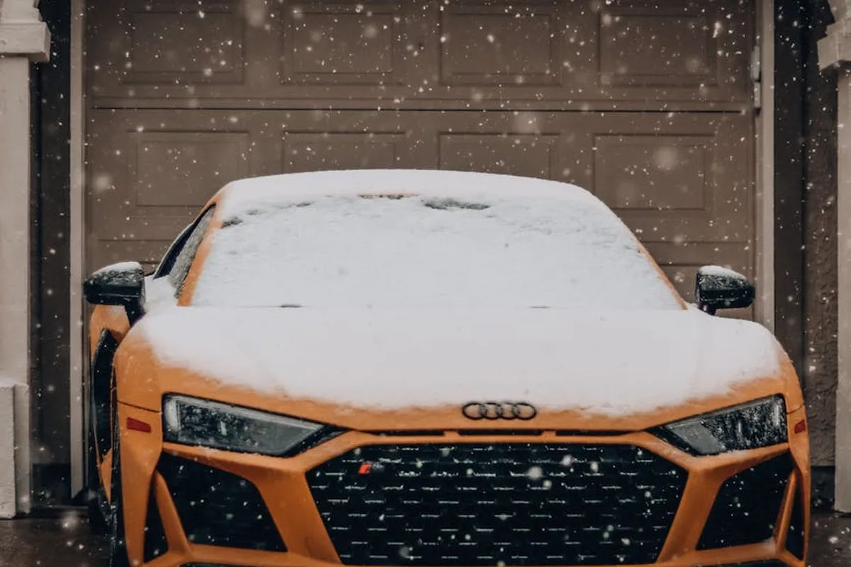 An orange car parked inside a snow-covered garage with the garage door closed.