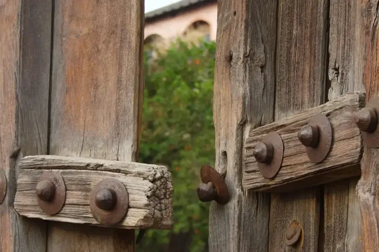 Weathered wooden gate with exposed bolts and hinges, illustrating manual operation without power
