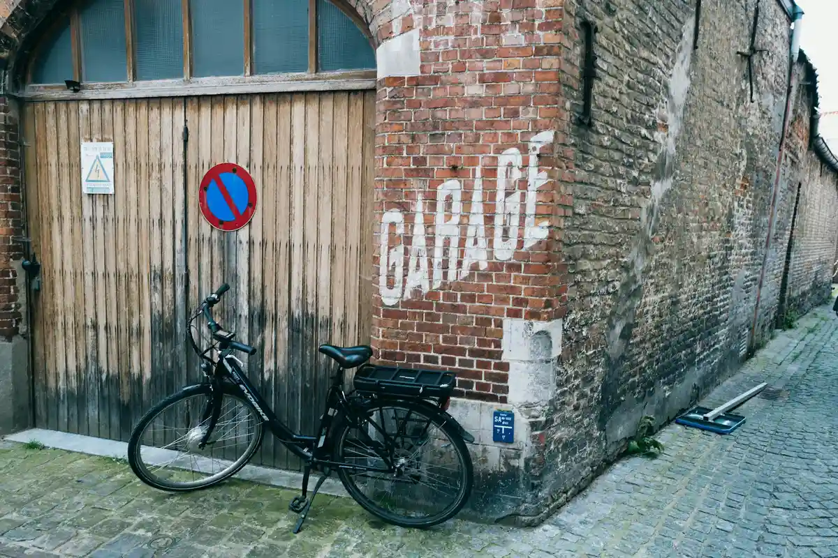 Brick-walled garage with a wooden door and a bicycle parked nearby, illustrating a work-ready setting for spring adjustment tools.