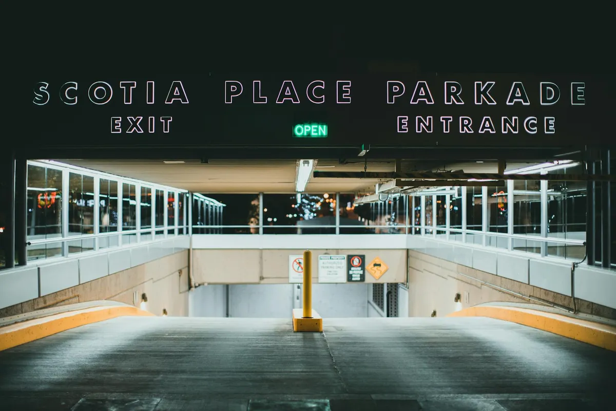 Underground parking garage entrance with an illuminated OPEN sign, descending ramp, and glass railings on both sides.