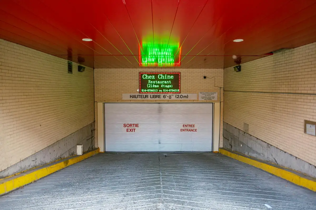 Underground parking garage entrance with a closed garage door, a green exit sign overhead, and signs on the door in multiple languages.