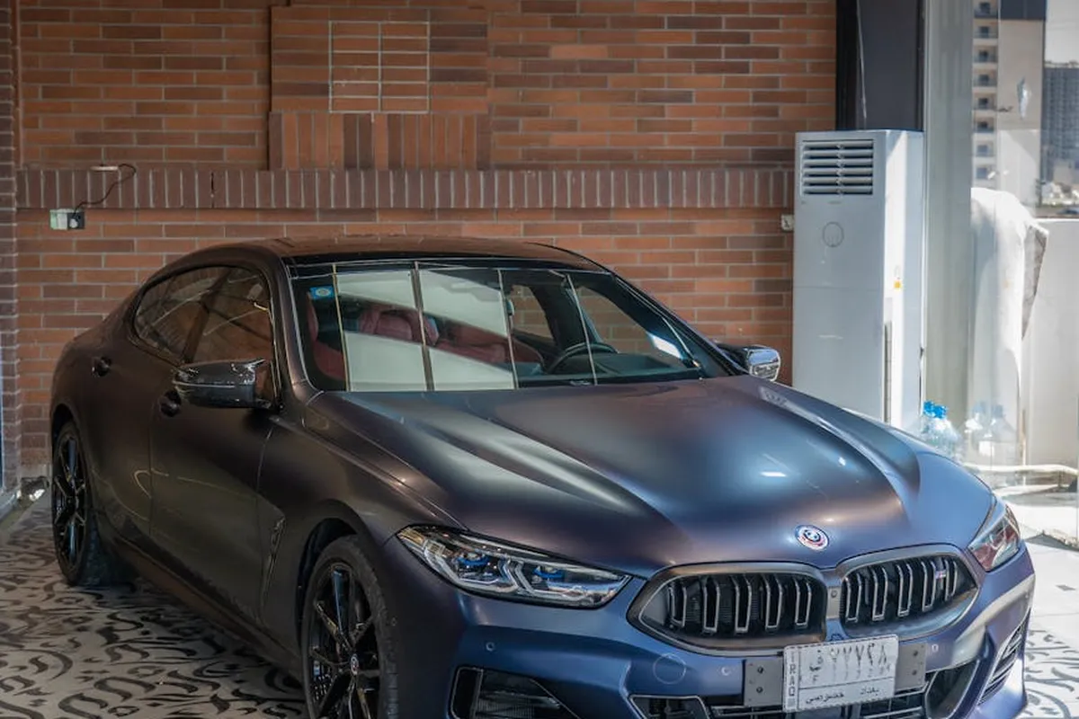 Blue BMW sedan parked in a residential garage with brick walls, a patterned floor, and utility equipment in the background.