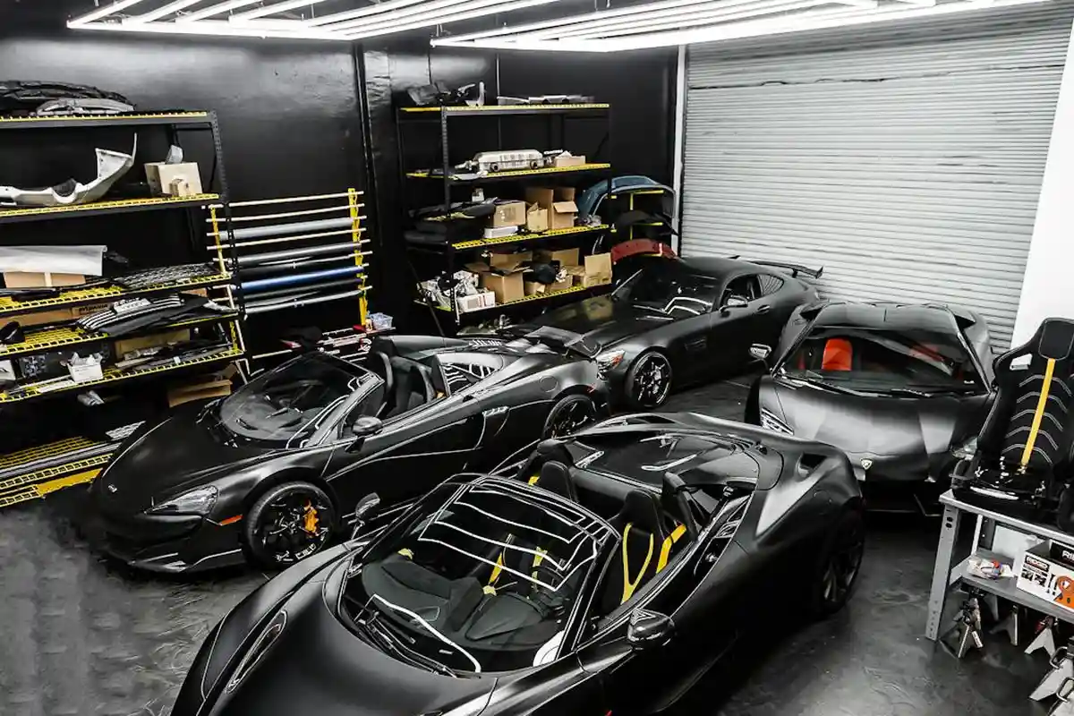 Interior of a finished garage with multiple high-end sports cars, organized storage shelves, and bright overhead lighting