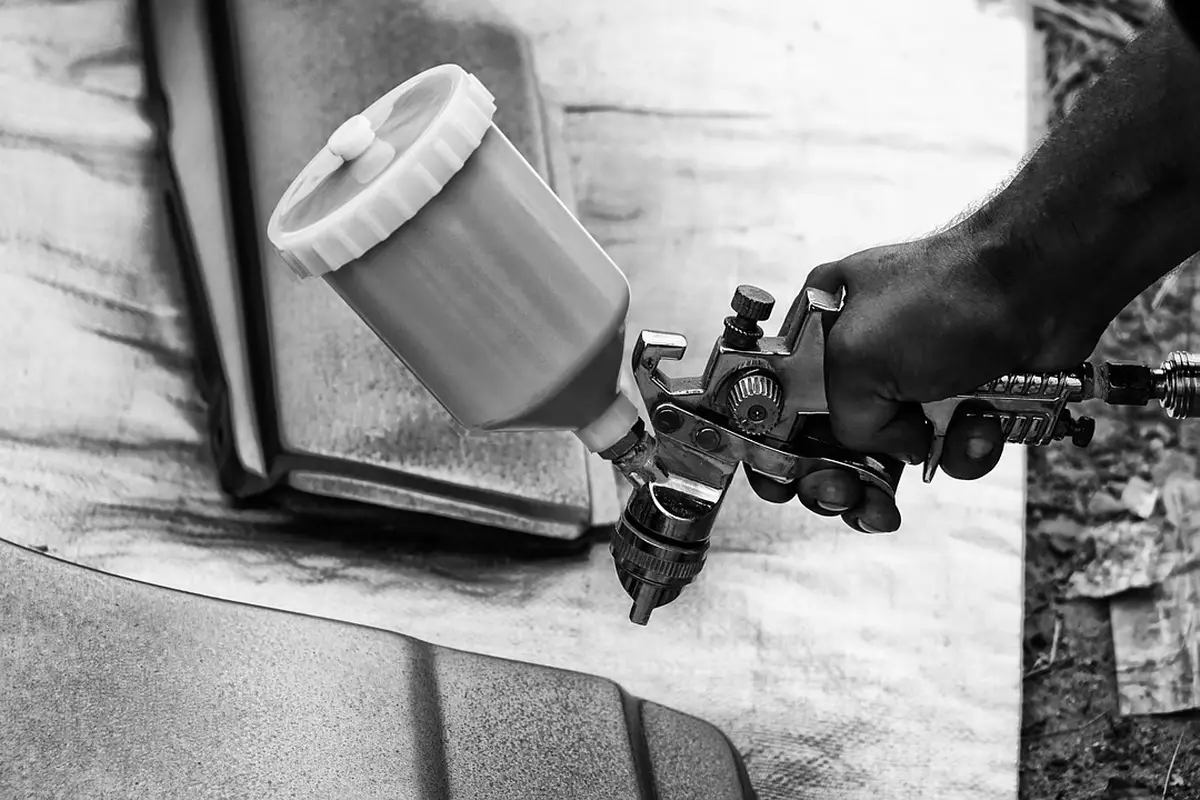 Black-and-white image of a hand holding a spray gun applying coating to a garage floor