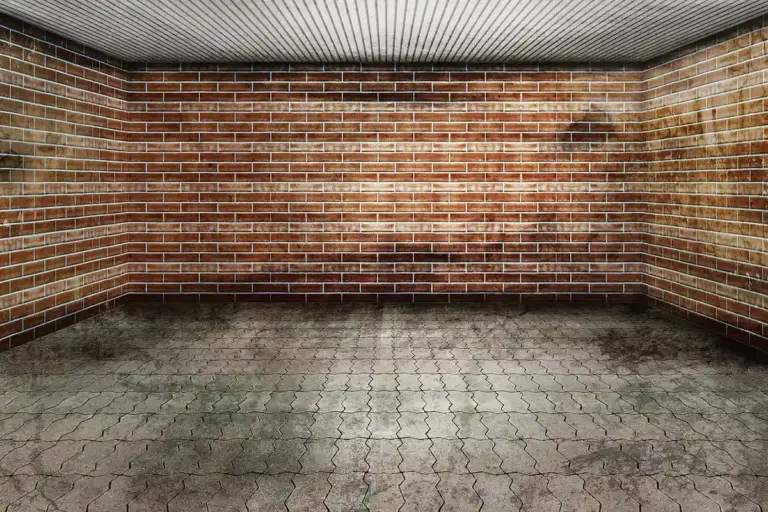 Empty garage with brick walls and a weathered interlocking tile-style floor.
