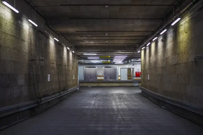Indoor garage tunnel with concrete walls and ceiling, lit by fluorescent lights along the sides.