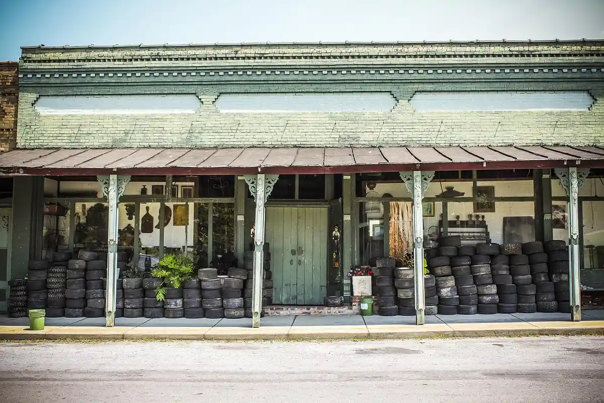 Weathered garage storefront with a green door and stacked tires along the front porch under a corrugated roof.