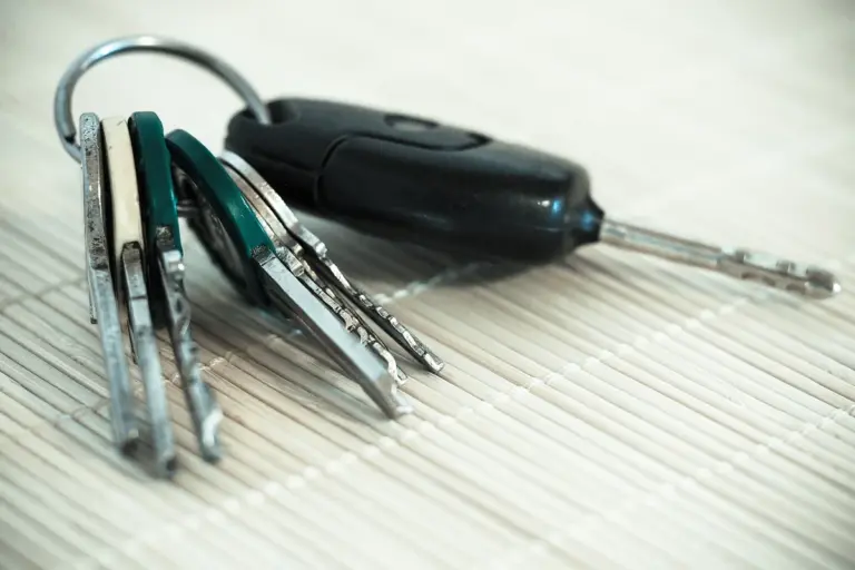 Close-up of a set of metal keys on a ring with a black key fob resting on a light wood surface.