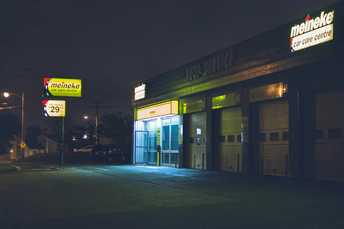 Nighttime exterior of a service garage with bright entryway and lit work bays, demonstrating focused task lighting for particular tasks.