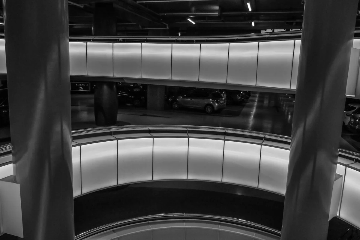 Black-and-white photo of a multi-level parking garage interior with curved ramps and overhead lighting, illustrating a workshop-ready environment for installing garage lighting.