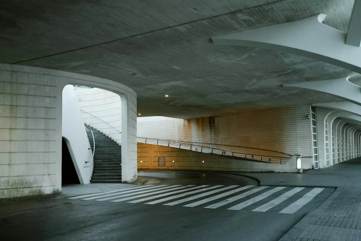 Concrete parking garage area with a stairwell to the left and a ramp; exposed edges and openings where mice could potentially enter.