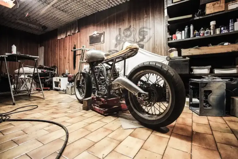 A vintage motorcycle on a maintenance stand inside a wooden garage, surrounded by tools, shelves, and organized storage.