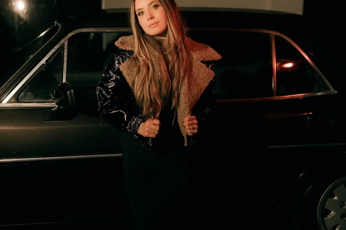 A woman stands next to a dark SUV in a dimly lit garage, preparing to troubleshoot garage door opener programming.