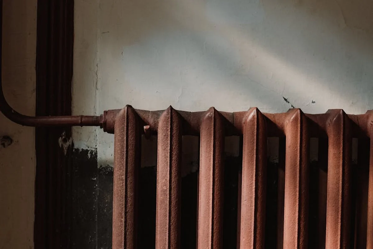 Rusty cast-iron radiator with a copper supply pipe running along the top in a garage.