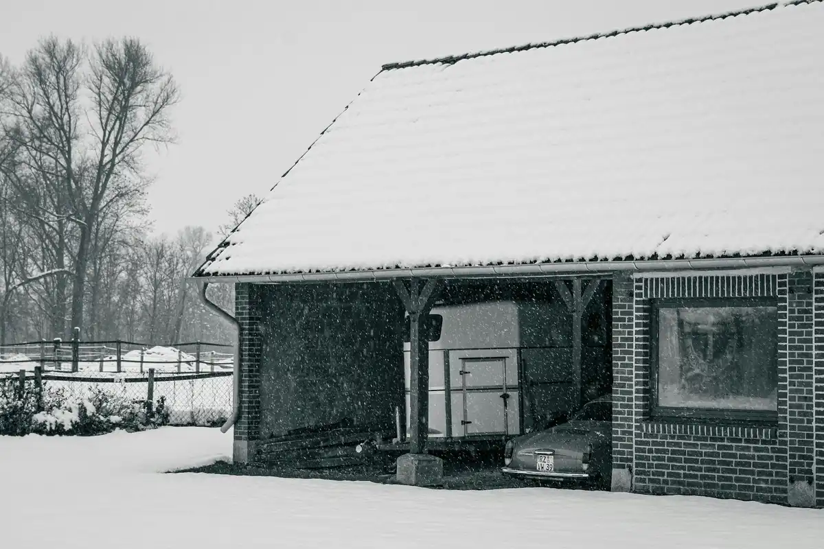 Snow-covered brick garage with a steep pitched roof; a car is parked in the sheltered bay.