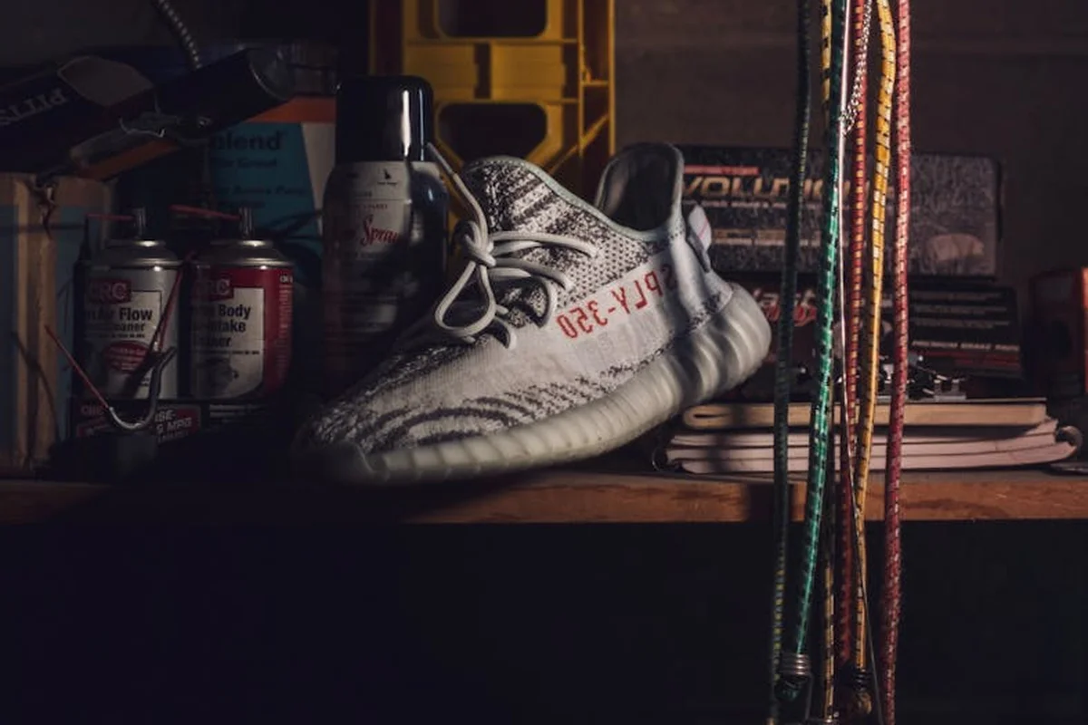 A white sneaker rests on a wooden workbench in a cluttered garage with cords and tools in the background.