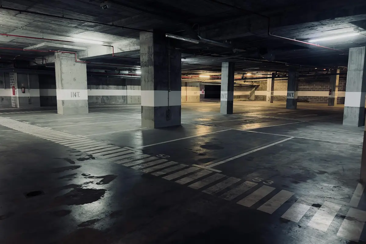 Empty multi-level garage with wet, stained concrete floor and supporting columns, illustrating areas where gasoline spills may occur.