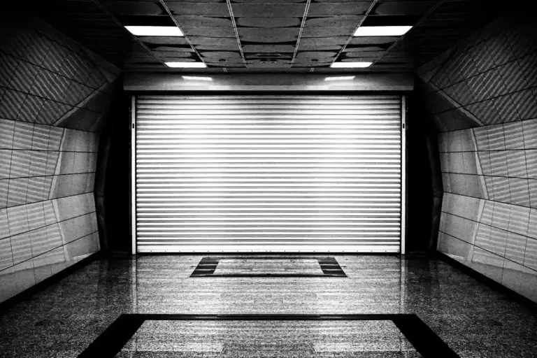 Black-and-white image of an empty garage with a closed roll-up door, illustrating a space suitable for installing a storm shelter.