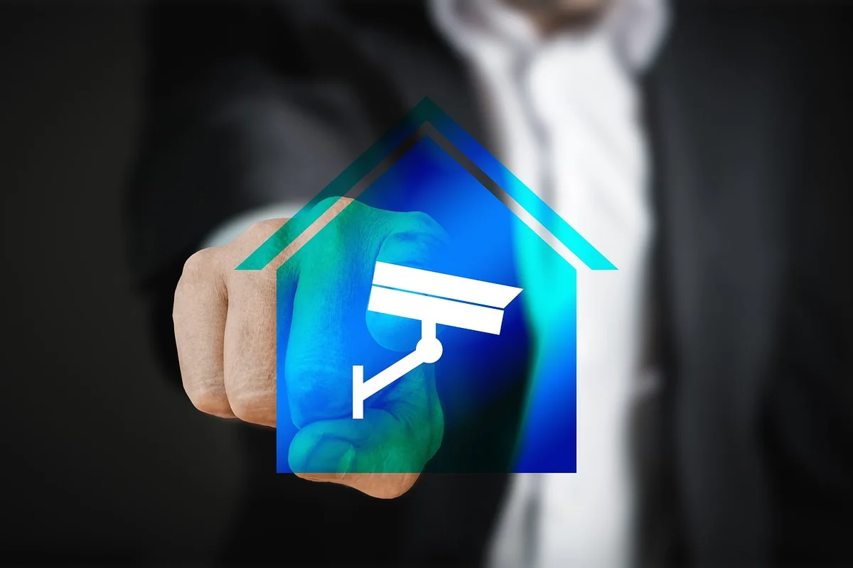 Close-up of a finger pressing a remote button with a digital overlay of a house and security camera, illustrating syncing garage door devices.