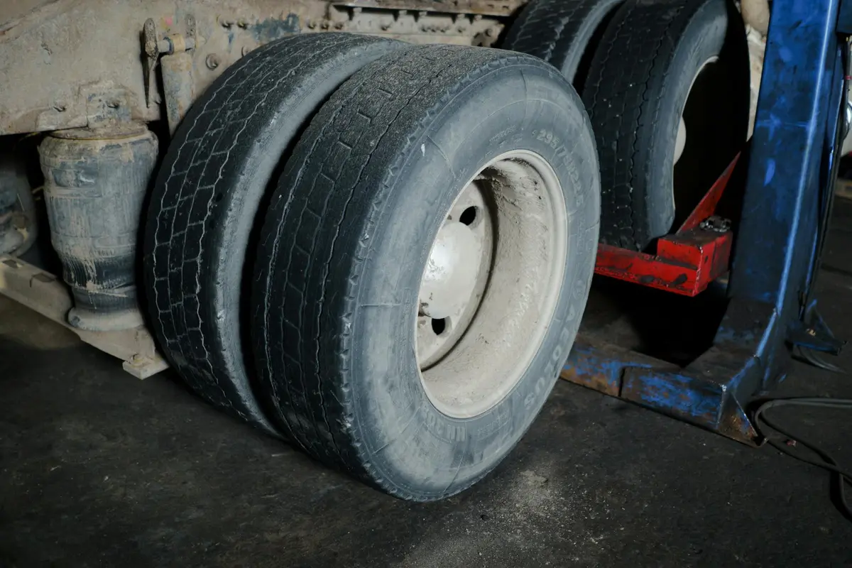 Large truck tire in a dusty garage with a dark concrete floor and nearby workshop equipment.