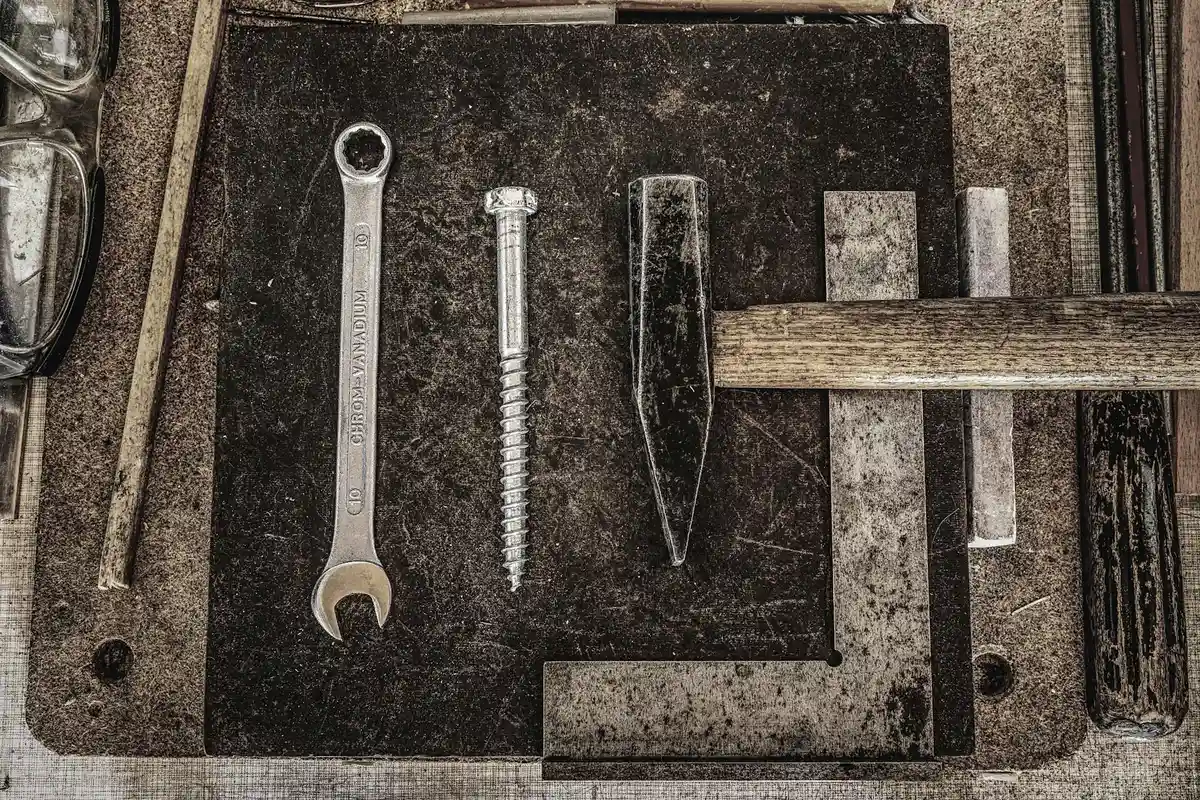 Weathered garage workbench with various hand tools laid out on a dark surface, including a wrench, bolt, chisel, and hammer